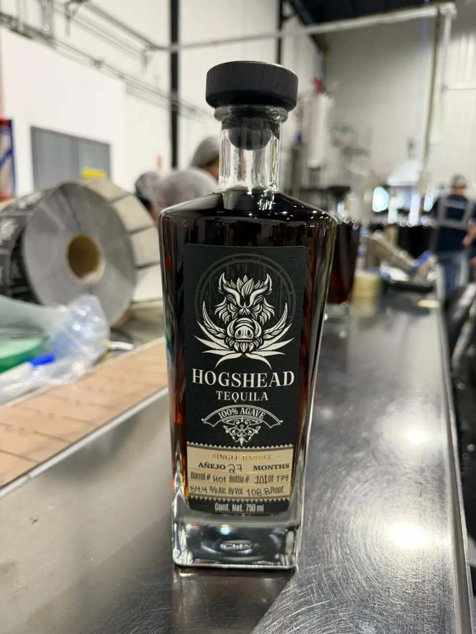 A finished Hogshead Travesía bottle on the line, its label filled in by hand: Añejo, 27 months, Barrel # H01, Bottle # 101 of 174, 54.4% alcohol by volume, 108.8 proof