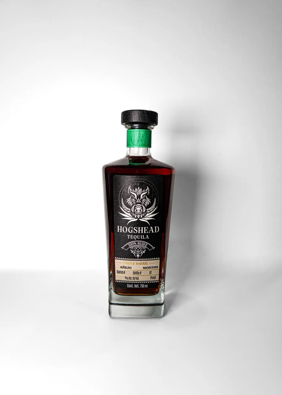 A bottle of Hogshead Tequila Single Barrel Añejo: black label with the boar emblem, HOGSHEAD TEQUILA, 100% agave, and a green neck
